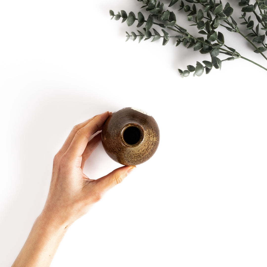 Hand holding a brown ceramic sake carafe with a subtle rabbit and moon design, viewed from above.