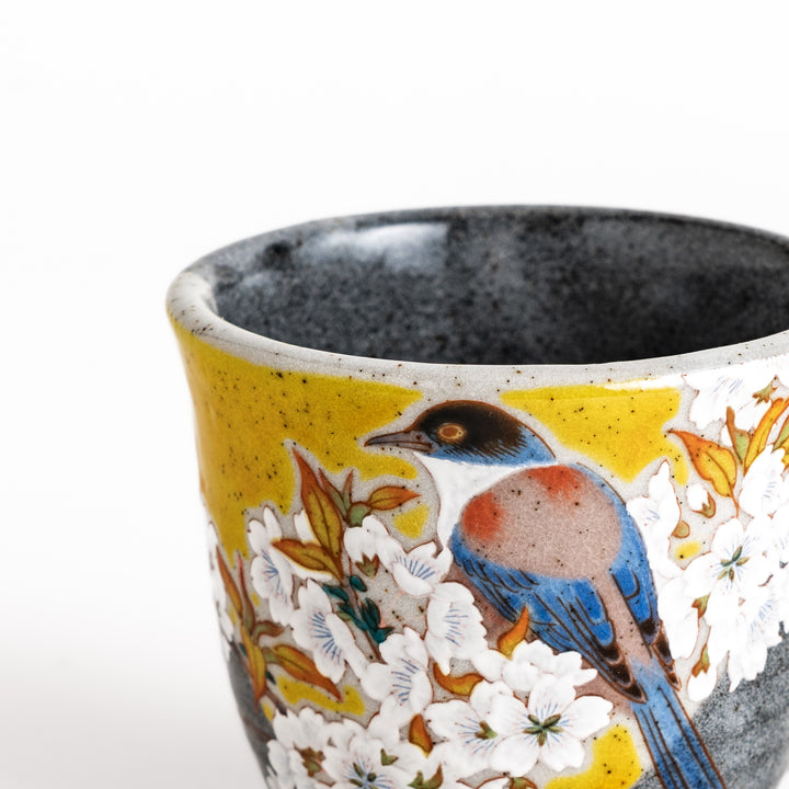 Ceramic mug with a striking design of a bird perched on a flowering branch against a yellow background, perfect for enjoying your favorite beverage.