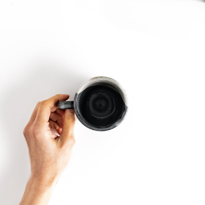 Hand holding a mug with a unique black and white glaze, viewed from above.