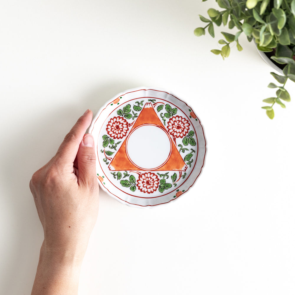 Hand holding a porcelain plate with a floral and geometric pattern, viewed from above, showcasing its detailed interior design.