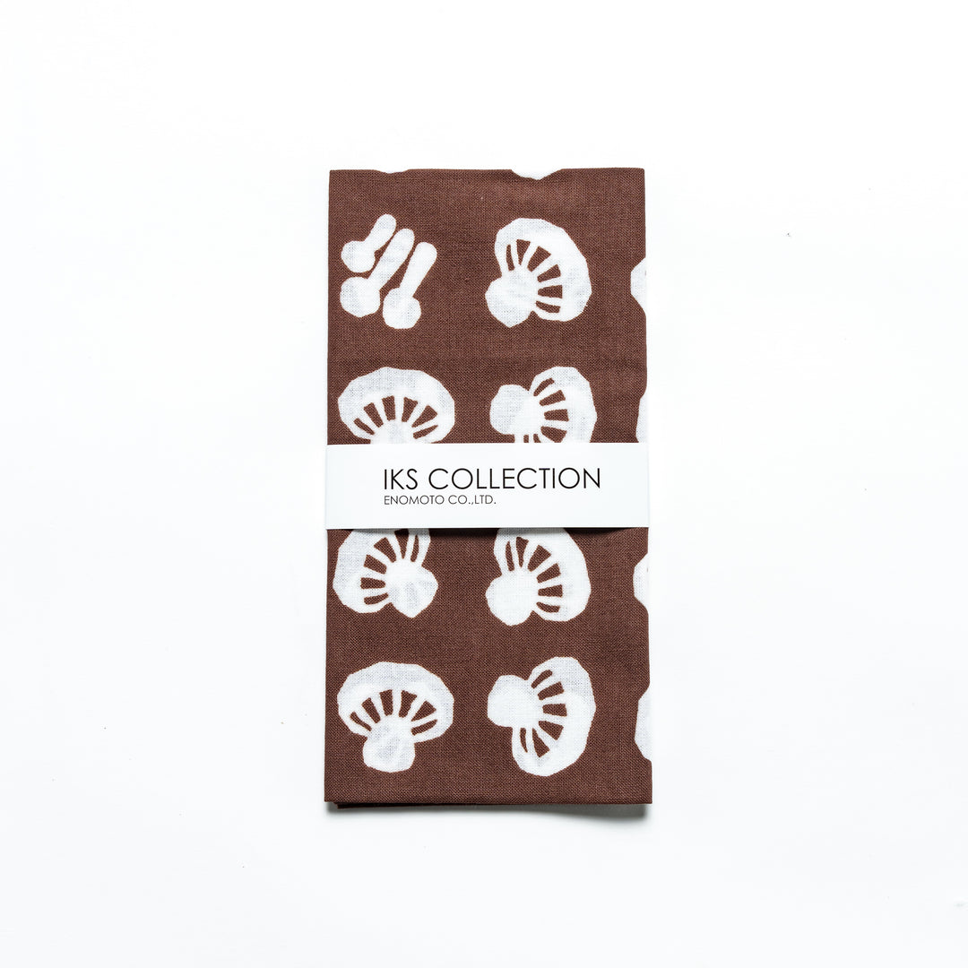 Folded brown tenugui with white mushroom patterns, wrapped in a branded sleeve.