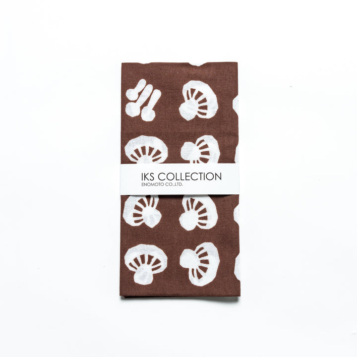 Folded brown tenugui with white mushroom patterns, wrapped in a branded sleeve.