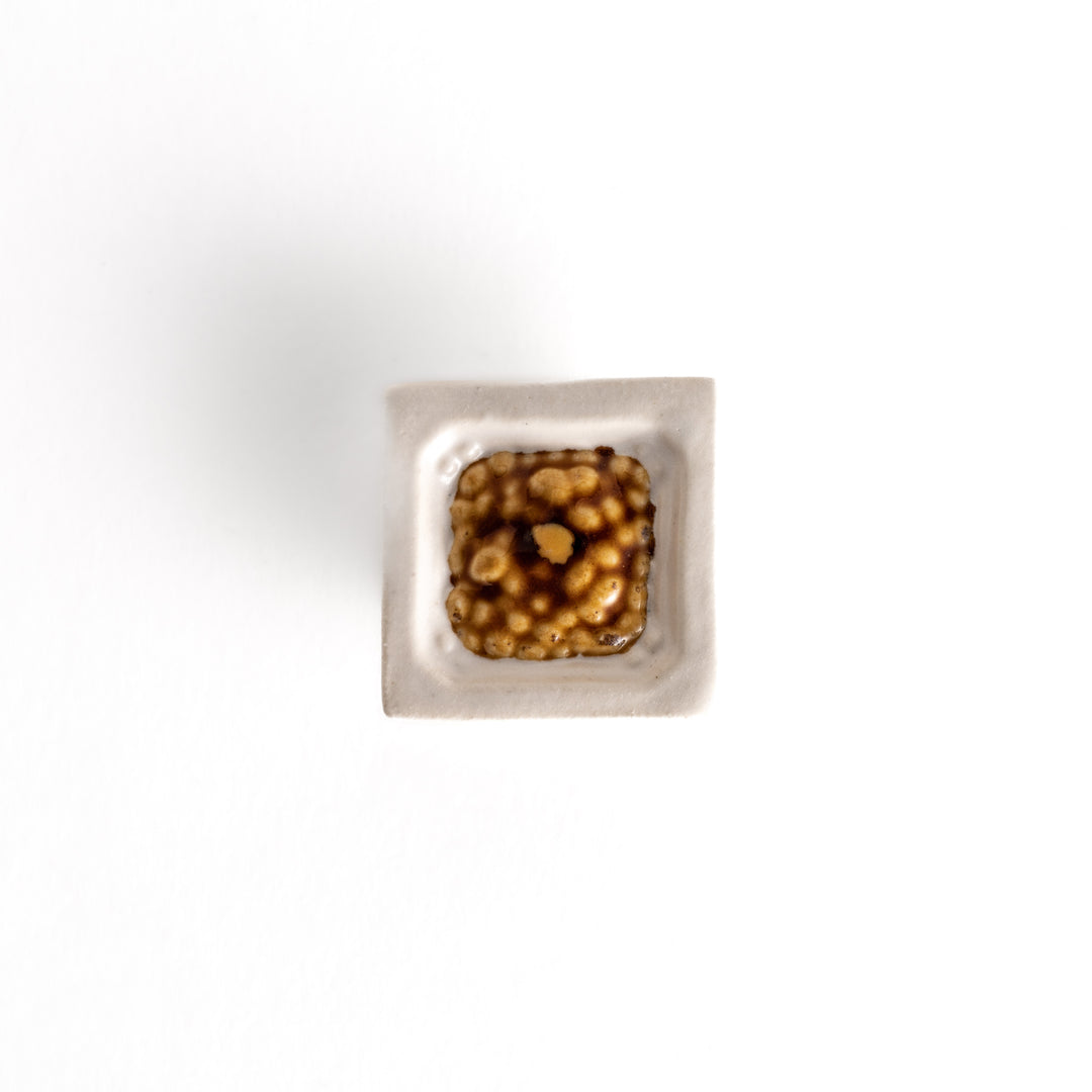 A top-down view of the square chopstick rest, showcasing its bowl-like shape and realistic natto bean texture.