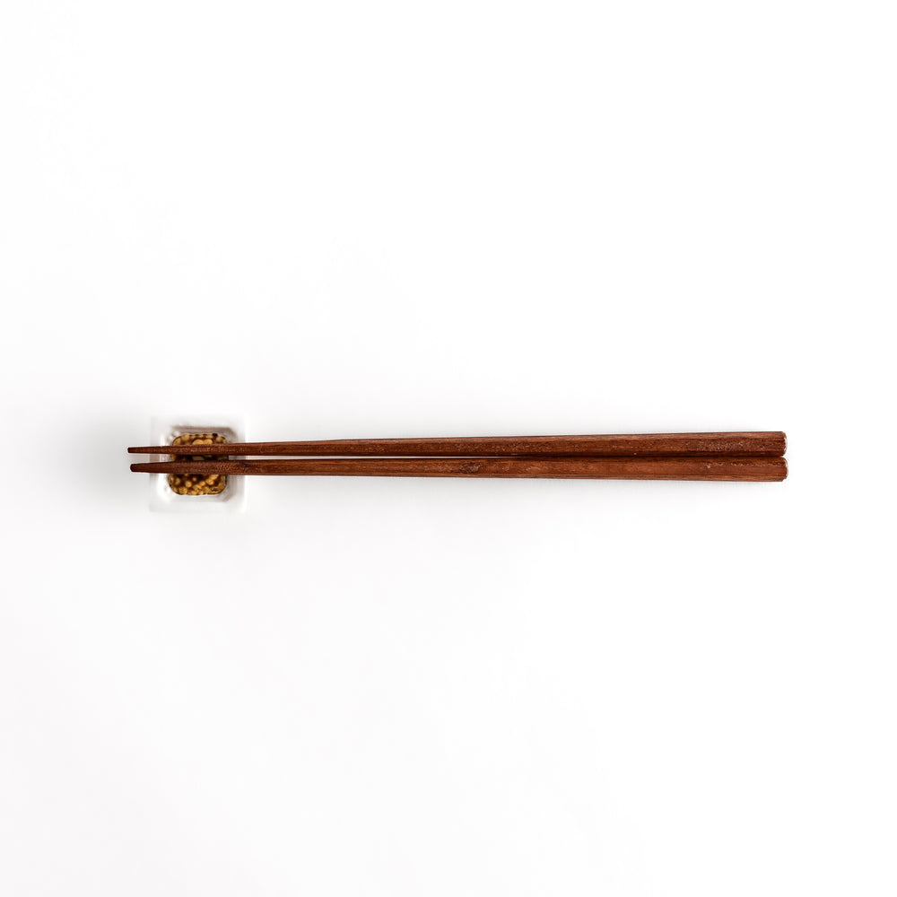 A pair of chopsticks resting on the natto-inspired square chopstick rest, displayed from a distance for an overall view.