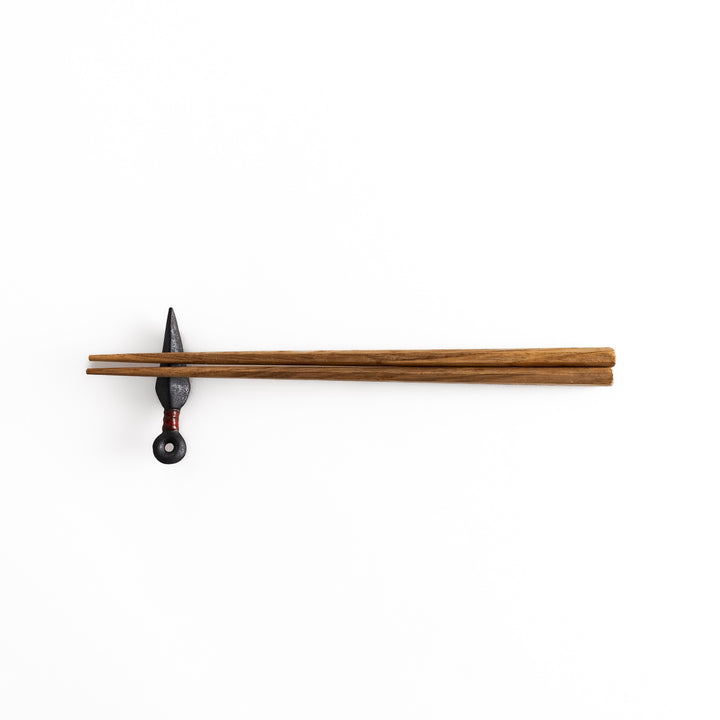 A pair of chopsticks resting on the kunai-shaped chopstick rest, displayed from a distance for overall view.