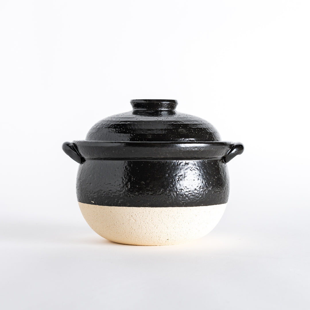 Side view of the donabe, displaying its rounded black body, white base, and glossy black lid.