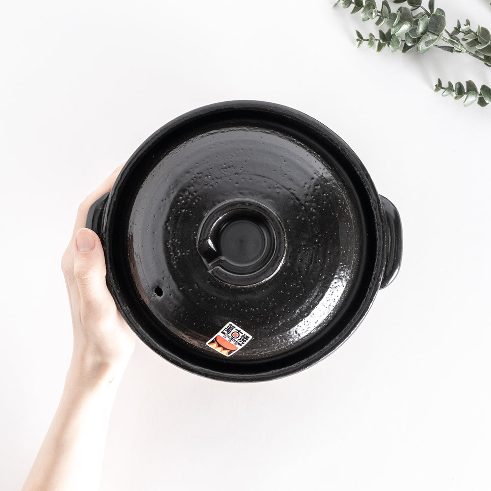 Top-down view of the donabe held by hand, showcasing its smooth black lid and centered handle.