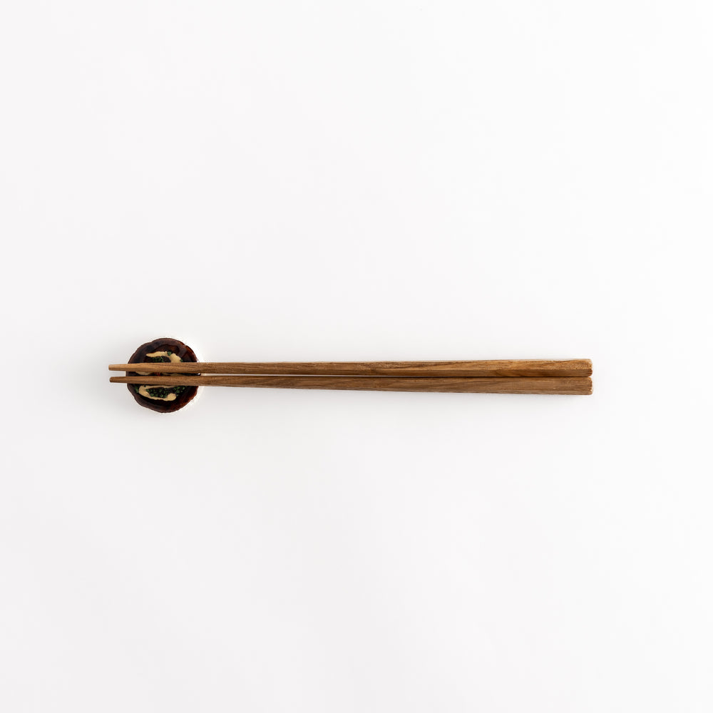 Pull-back view of the okonomiyaki-shaped chopstick rest with chopsticks resting on it, highlighting its playful design.