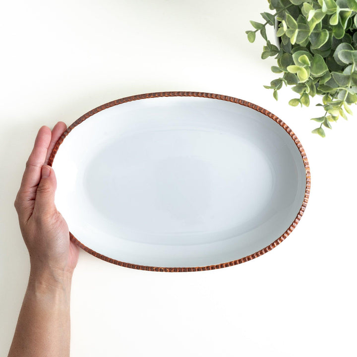 An oval-shaped white dinner plate with a rustic scallop-edged design. The border comes in blue, brown, and olive.