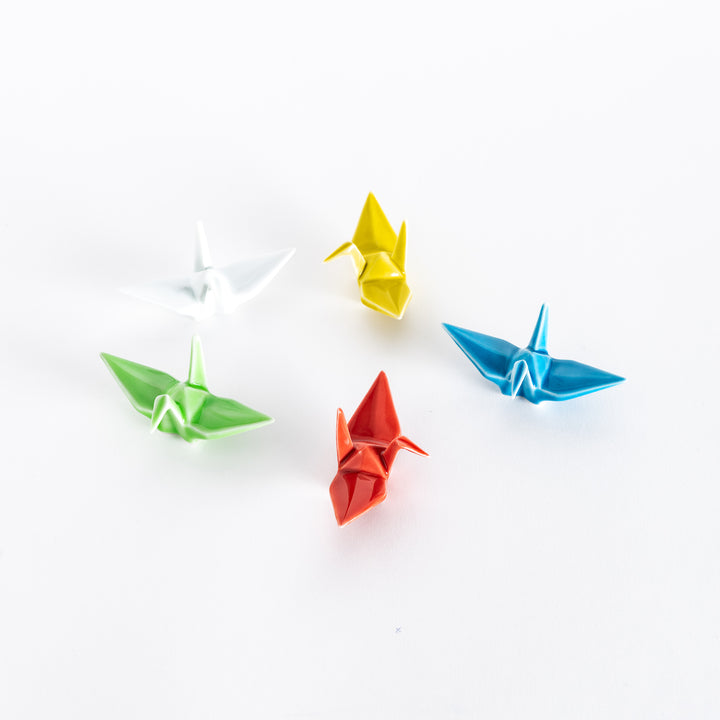 Top view of five ceramic crane-shaped chopstick rests in various colors, positioned in a circular arrangement on a white surface.