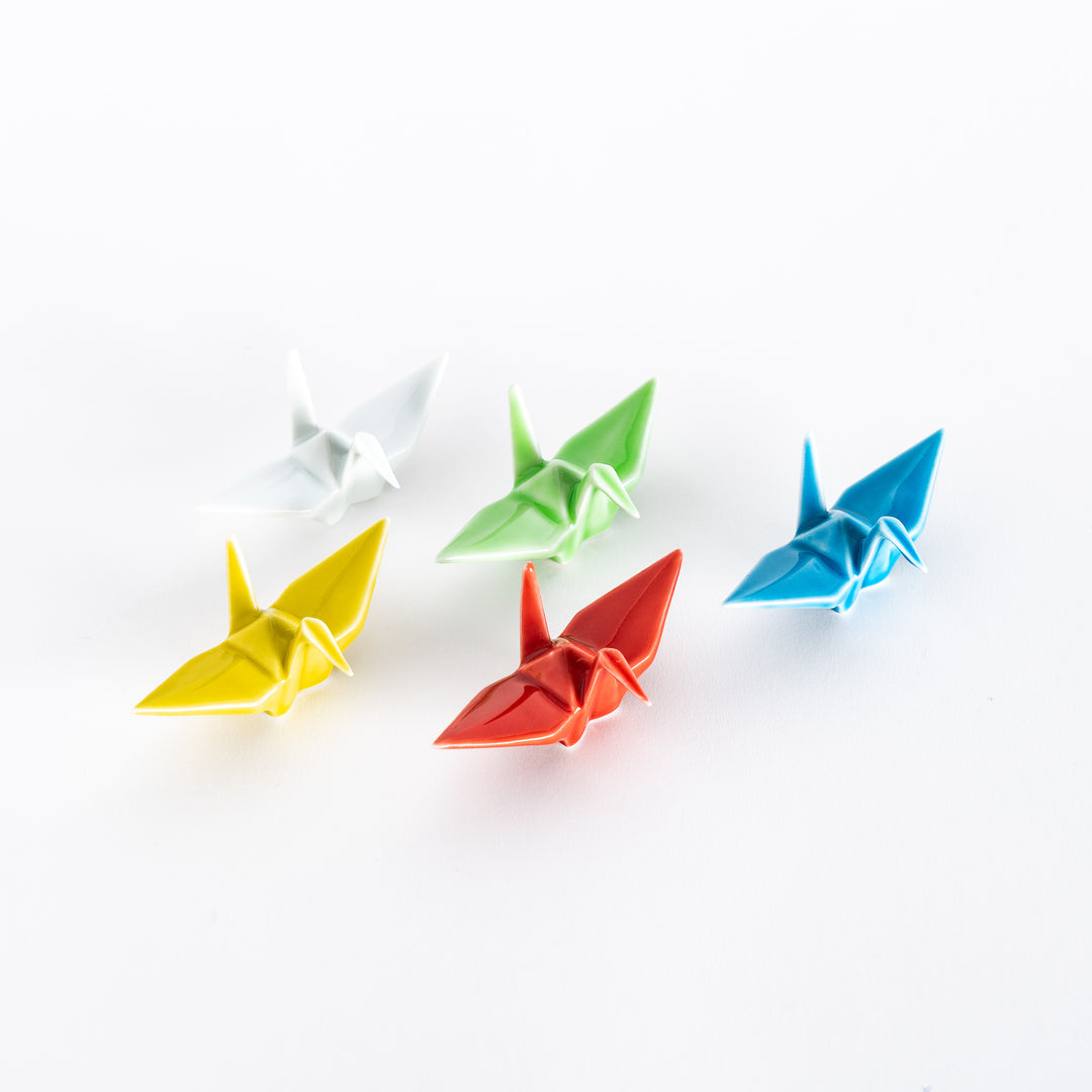 Five colorful ceramic crane-shaped chopstick rests in white, green, yellow, red, and blue arranged on a white background.