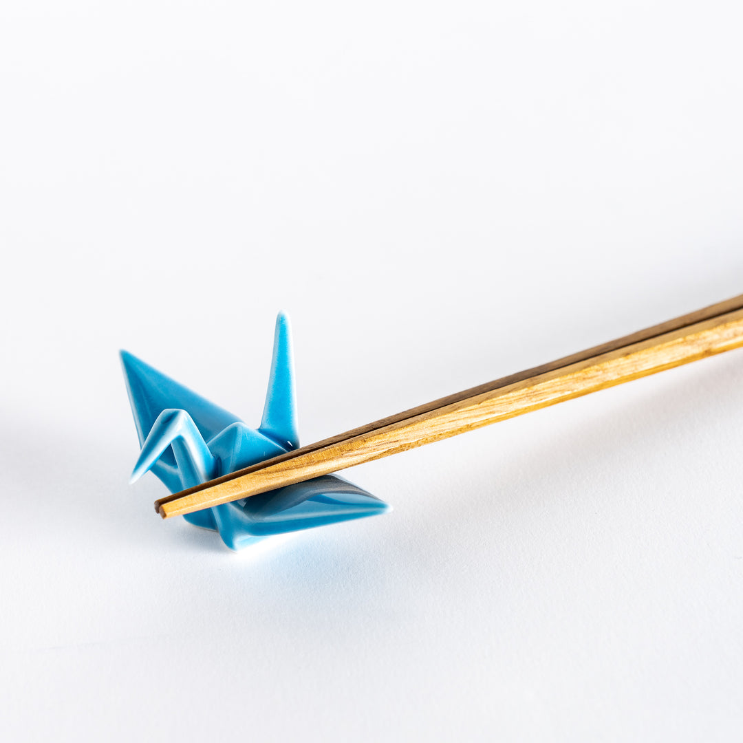 Close-up of chopsticks resting on the light blue ceramic crane-shaped chopstick rest.