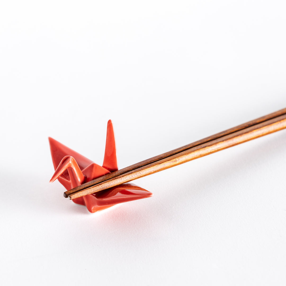 Close-up of chopsticks resting on the red ceramic crane-shaped chopstick rest.