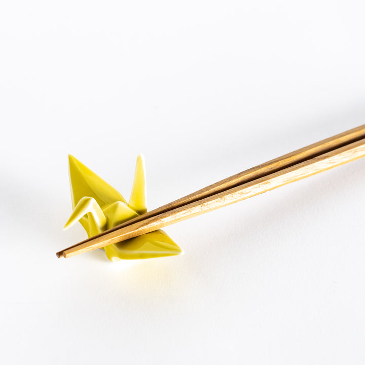 Close-up of chopsticks resting on the yellow ceramic crane-shaped chopstick rest.