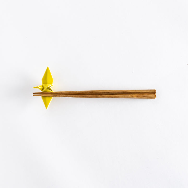 Wide view of chopsticks resting on the yellow ceramic crane-shaped chopstick rest.