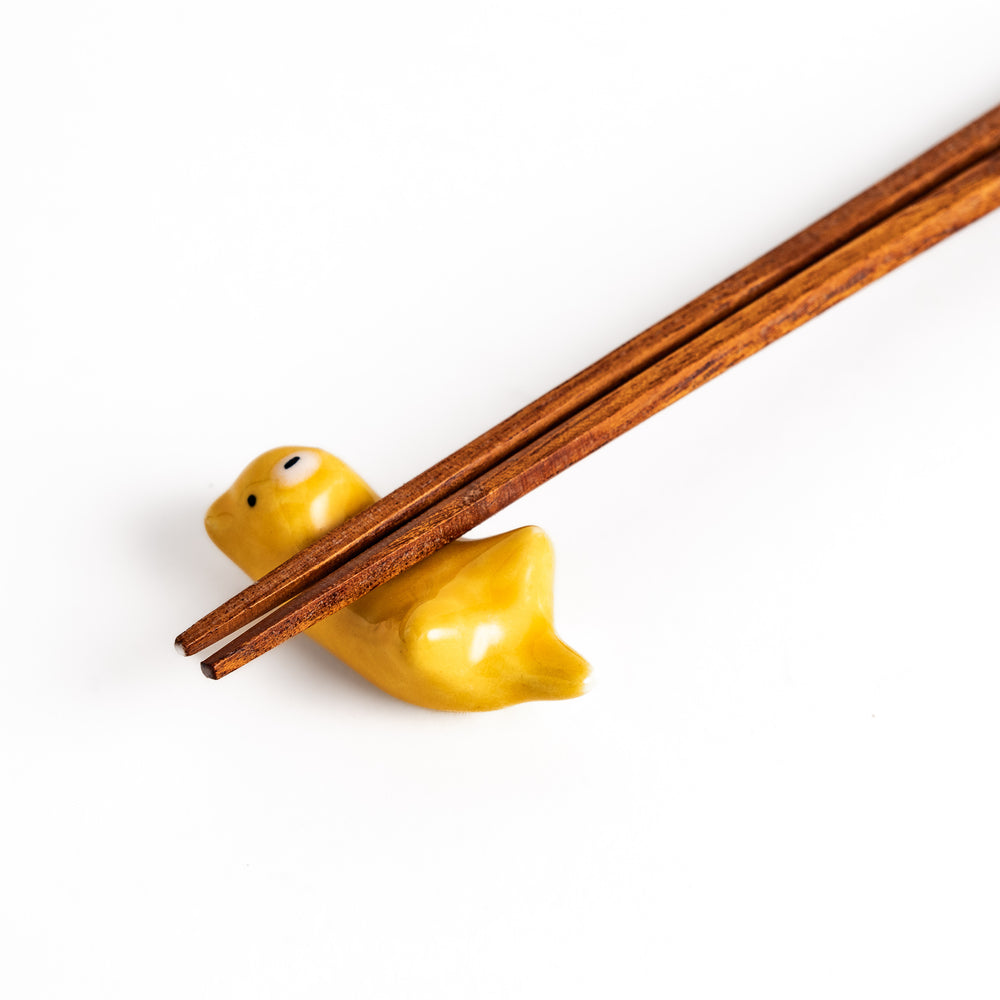 Otter Chopstick Rest holding wooden chopsticks, showcasing its playful and functional design with a glossy yellow finish.