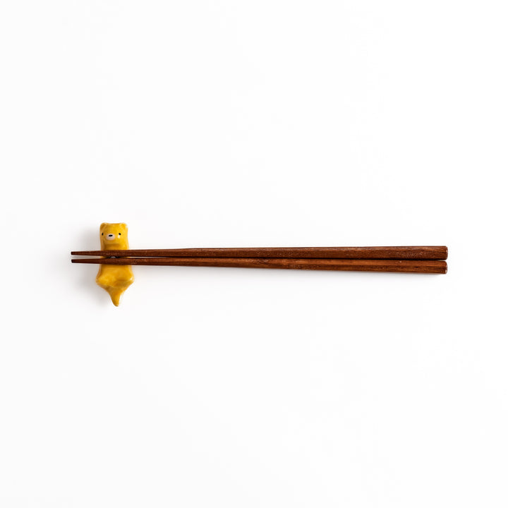 Otter Chopstick Rest holding wooden chopsticks, showcasing its playful and functional design with a glossy yellow finish.