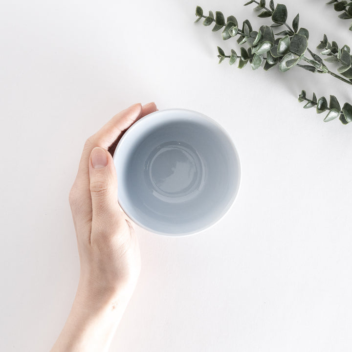 A light blue dessert bowl held by hand, viewed from above, emphasizing its glossy, rounded interior.