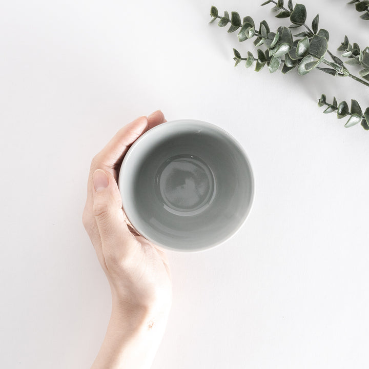 A pastel gray dessert bowl held by hand, viewed from above, showcasing its glossy, rounded interior.