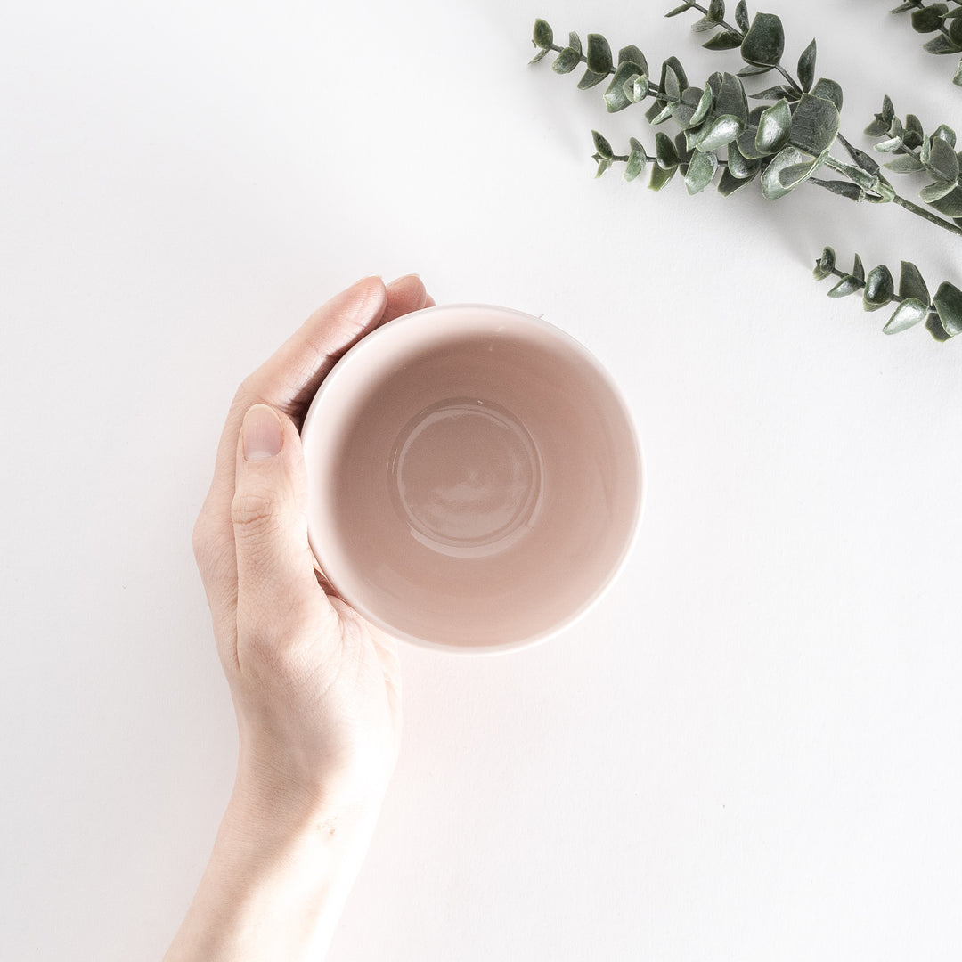 A soft pink dessert bowl held by hand, viewed directly from above, showing its round, glossy interior.