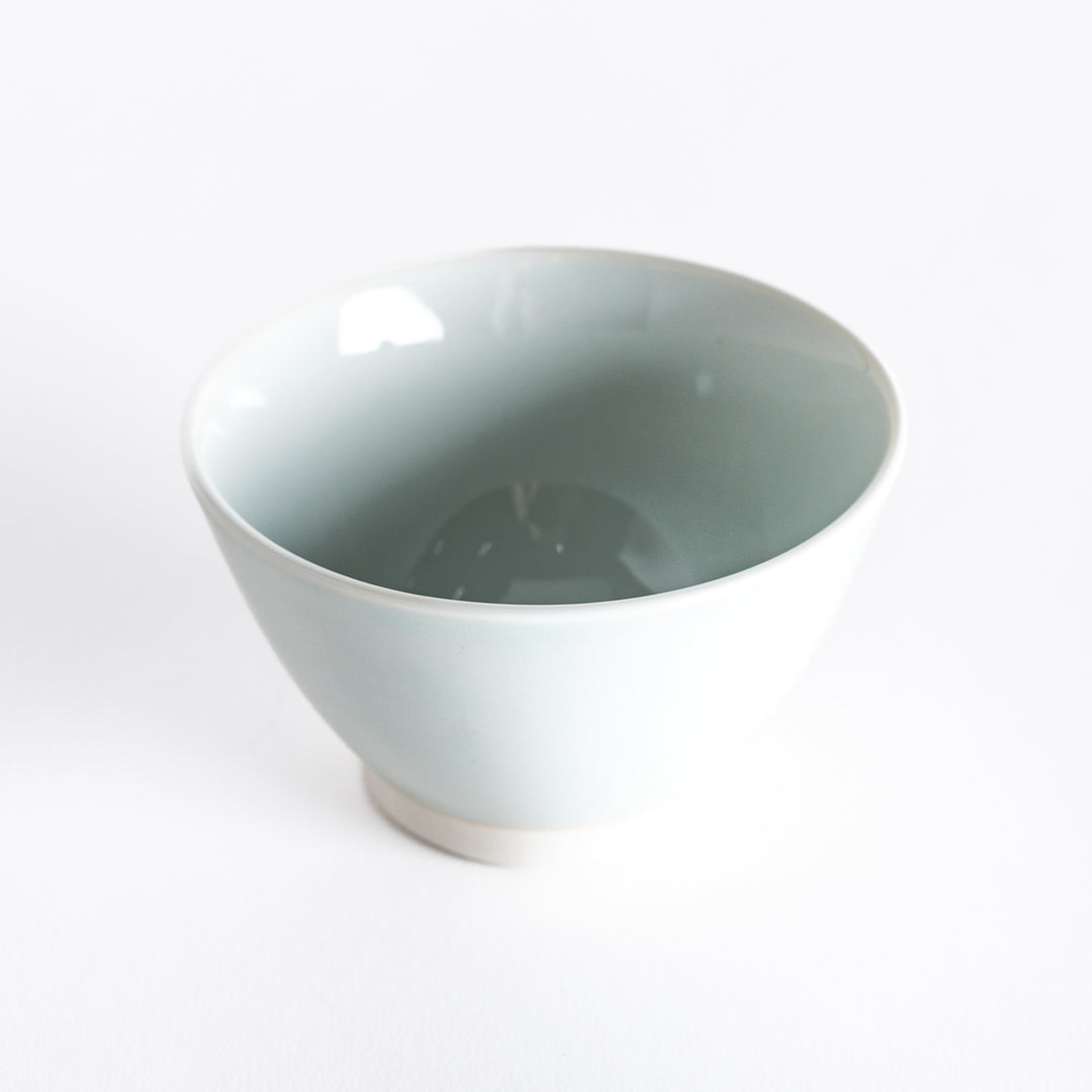 A blue-tinted white dessert bowl, photographed at a slight angle, showcasing its understated elegance and gentle curves.