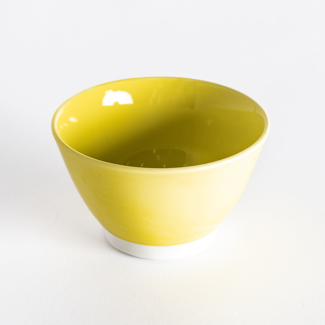 A bright yellow dessert bowl held by hand, viewed from above, showing its vibrant, round interior.