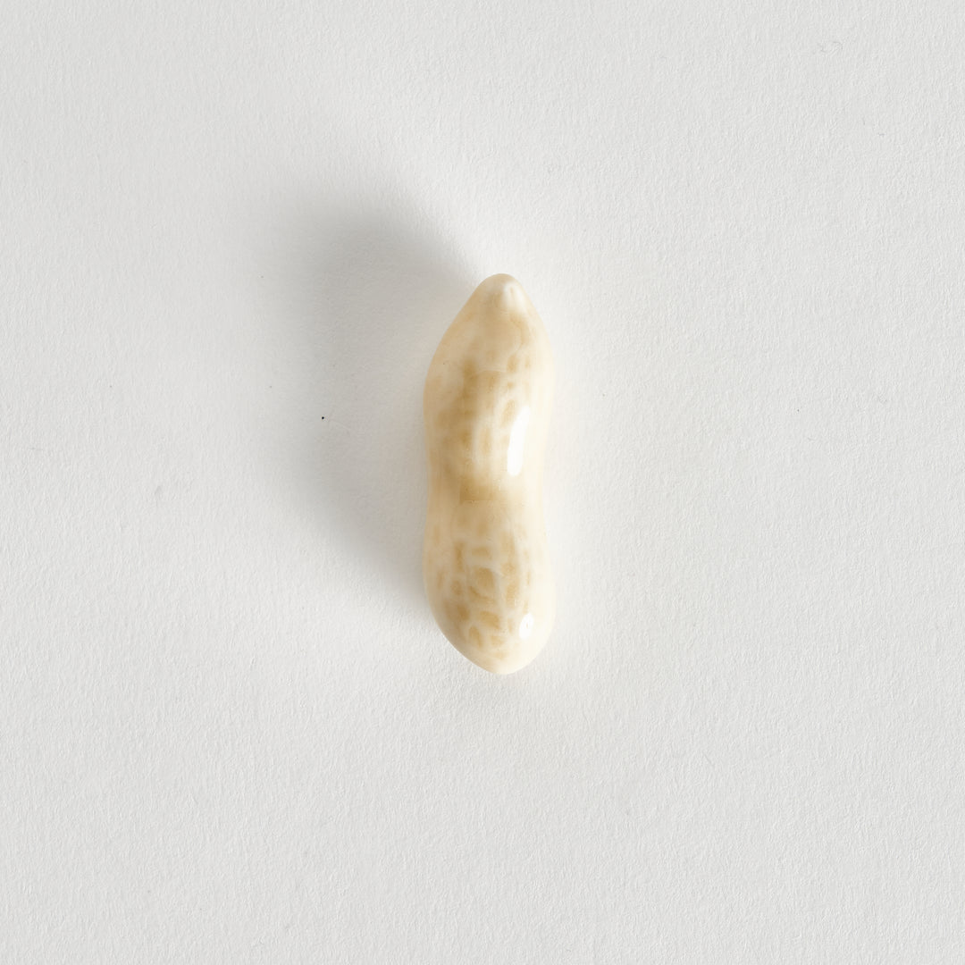 A close-up of a light-colored peanut on a white background, showing its textured surface.