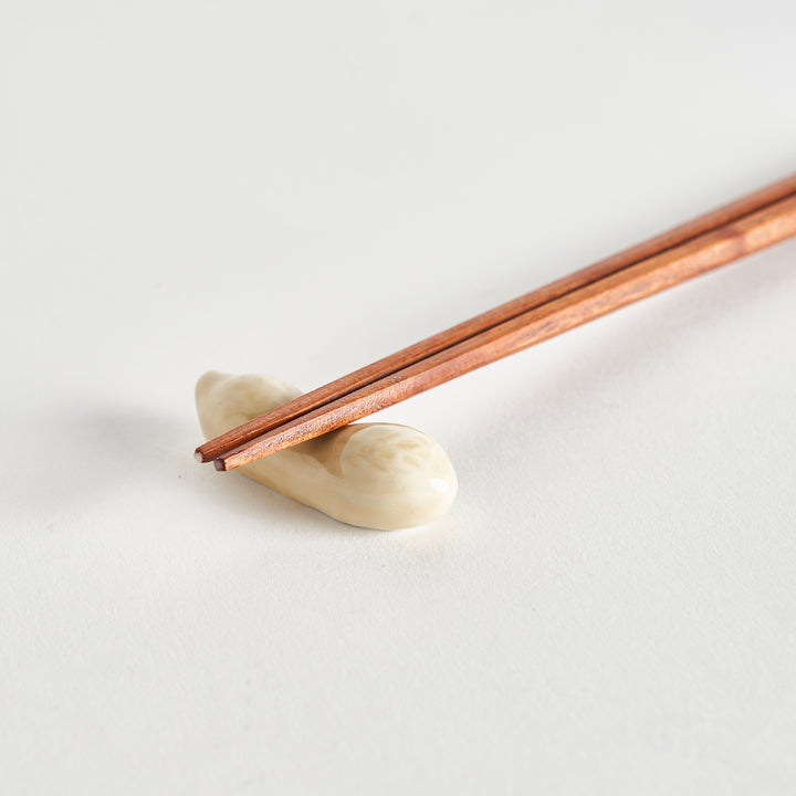 A pair of chopsticks picking up the light-colored peanut from the white surface.