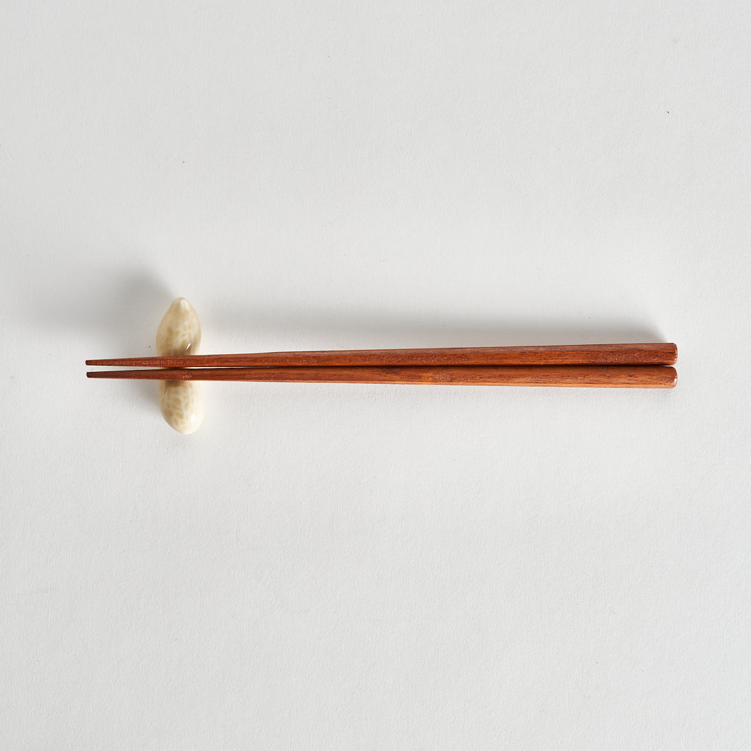 Top view of a single light-colored peanut with chopsticks placed across it, positioned on the white surface.