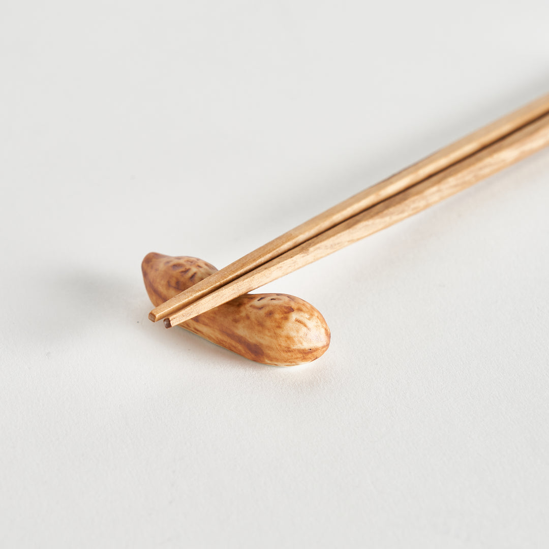 Wooden chopsticks gently resting on a light brown peanut-shaped chopstick rest, showcasing realistic textures.