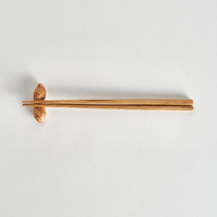 Top-down view of a single peanut chopstick rest, positioned with wooden chopsticks placed beside it.