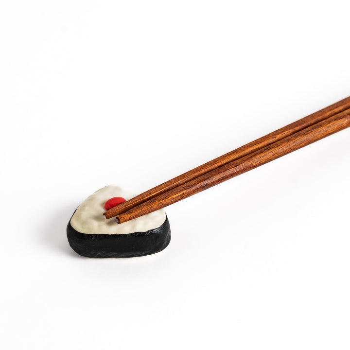 Pickled Plum Onigiri Chopstick Rest holding wooden chopsticks, showcasing its charming rice ball design and practical functionality.