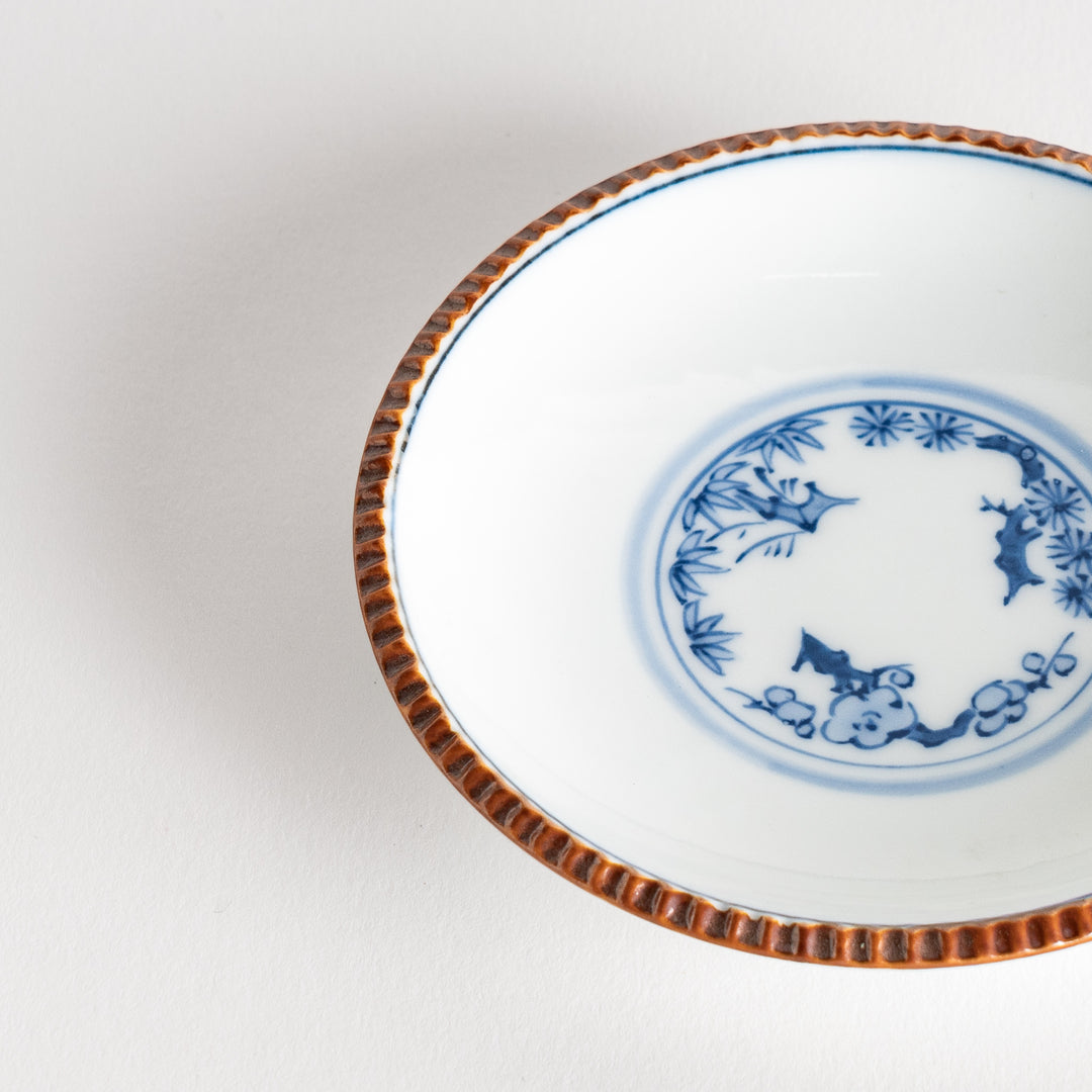 A small ceramic plate with a central blue floral motif surrounded by a white background, framed by a copper-colored textured rim.