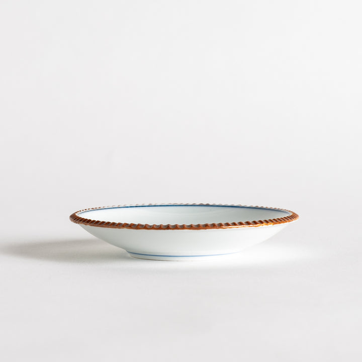 A small ceramic plate with a central blue floral motif surrounded by a white background, framed by a copper-colored textured rim.