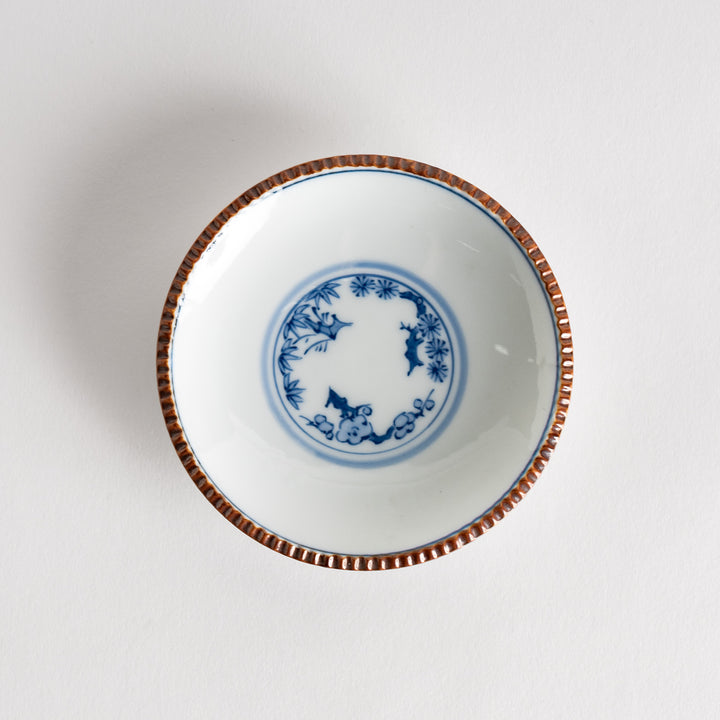 A small ceramic plate with a central blue floral motif surrounded by a white background, framed by a copper-colored textured rim.