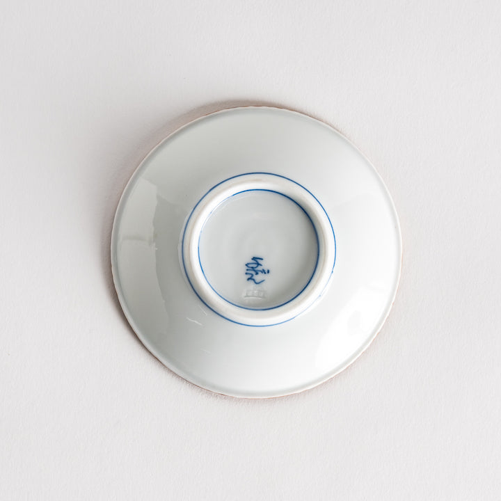 A small ceramic plate with a central blue floral motif surrounded by a white background, framed by a copper-colored textured rim.