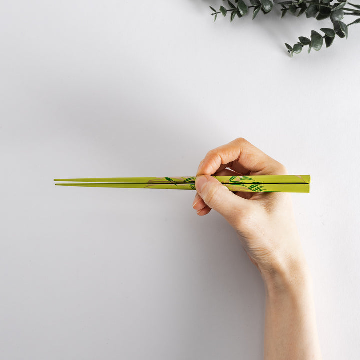 Green chopsticks with a bamboo pattern held in hand, showcasing a natural and elegant design.