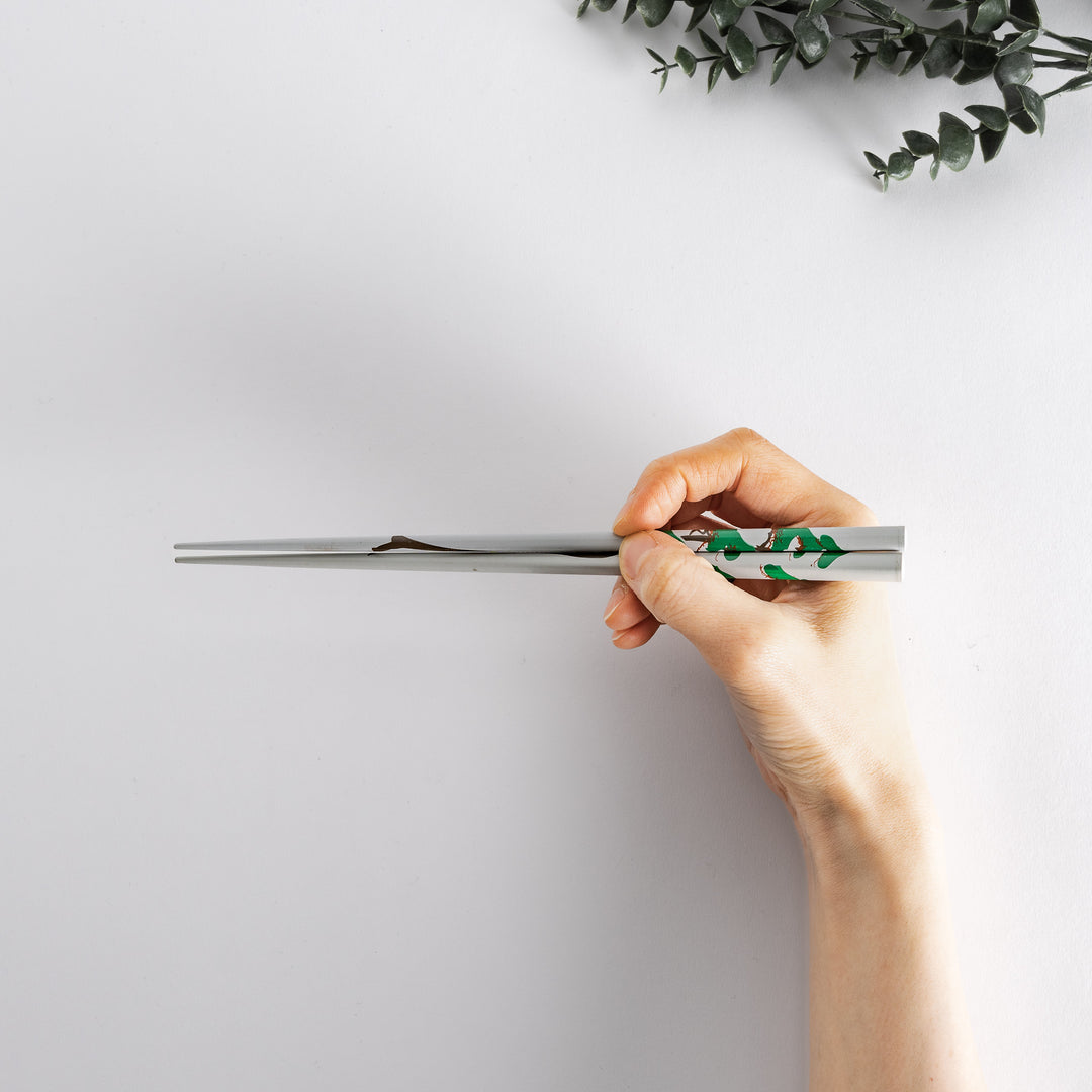 Gray chopsticks with a pine tree pattern held in hand, featuring a traditional and sophisticated motif.