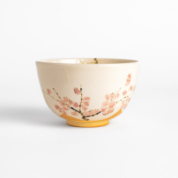 Plum Blossom Matcha Bowl with delicate pink floral designs on a cream-colored surface, perfect for enjoying matcha with a touch of elegance.