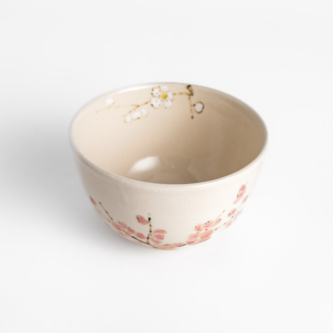 Plum Blossom Matcha Bowl with delicate pink floral designs on a cream-colored surface, perfect for enjoying matcha with a touch of elegance.