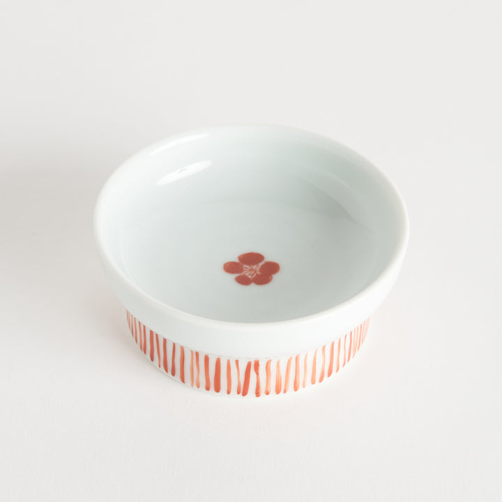 A small porcelain dish with a red plum blossom pattern and vertical red lines around the base.