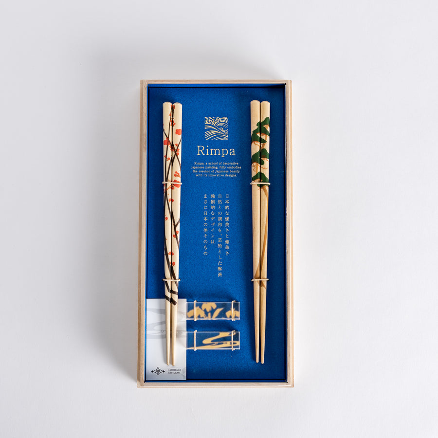 Elegant chopsticks with plum and pine designs, beautifully presented in a wooden box with a blue background.