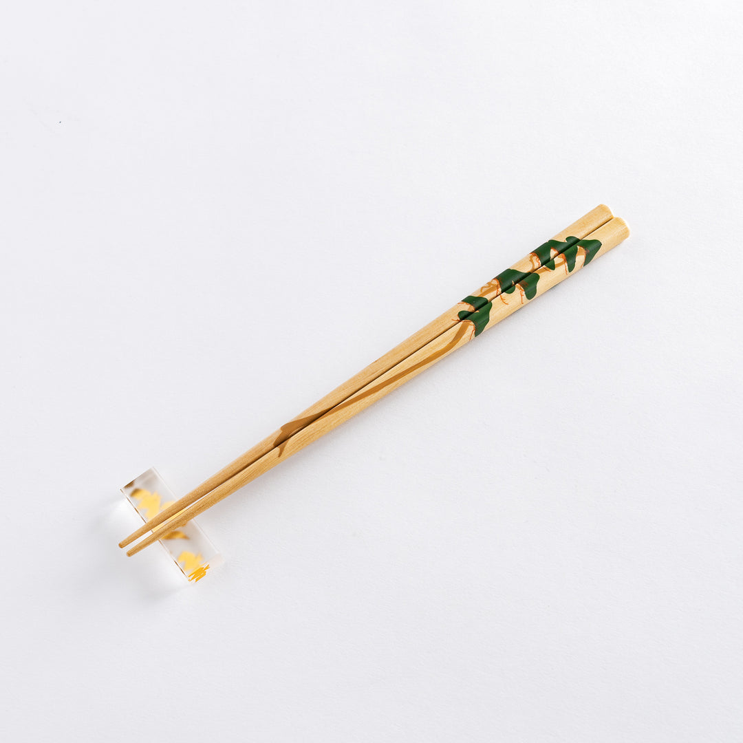 A close-up of a chopstick with a red plum blossom design, highlighting the intricate details on a light wooden finish.