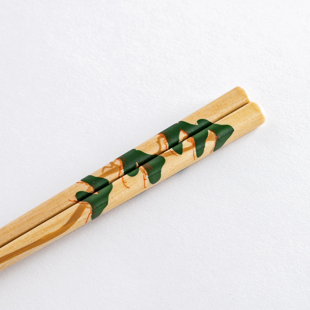 Chopsticks with a red plum blossom design resting on a clear chopstick holder with gold accents.