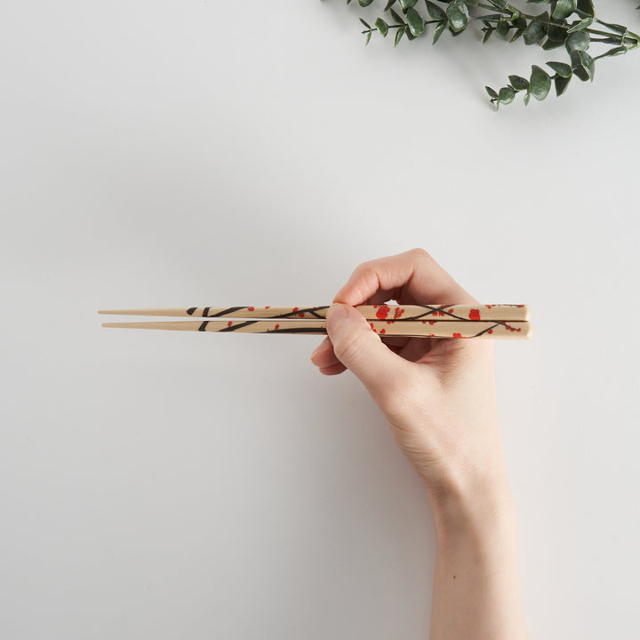 A hand holding a pair of chopsticks featuring a delicate plum blossom design, showcasing the craftsmanship and detail.