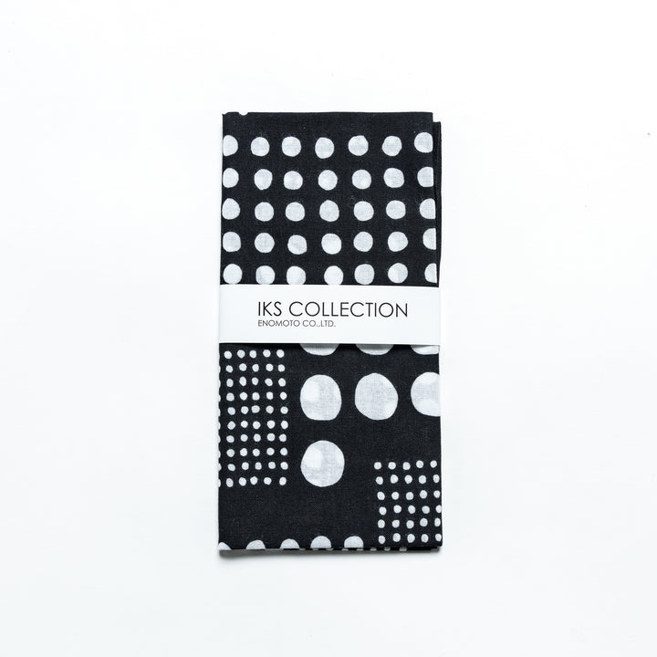 Black polka dot tenugui hand towel folded and wrapped in a product sleeve for display.