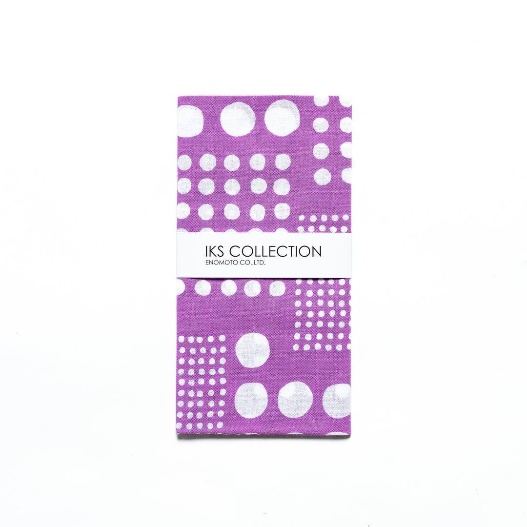 Purple polka dot tenugui hand towel folded and wrapped in a product sleeve for display.