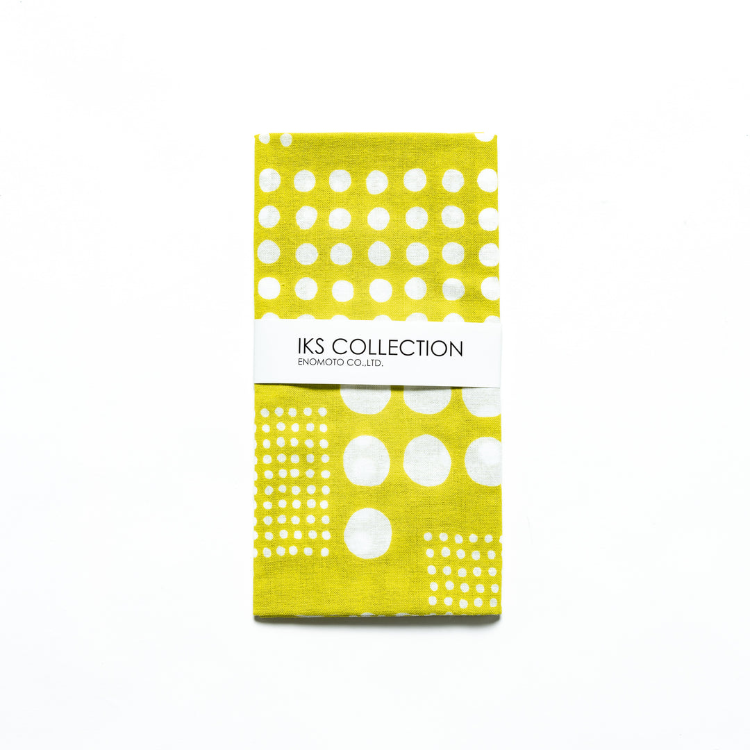 Yellow green polka dot tenugui hand towel folded and wrapped in a product sleeve for display.