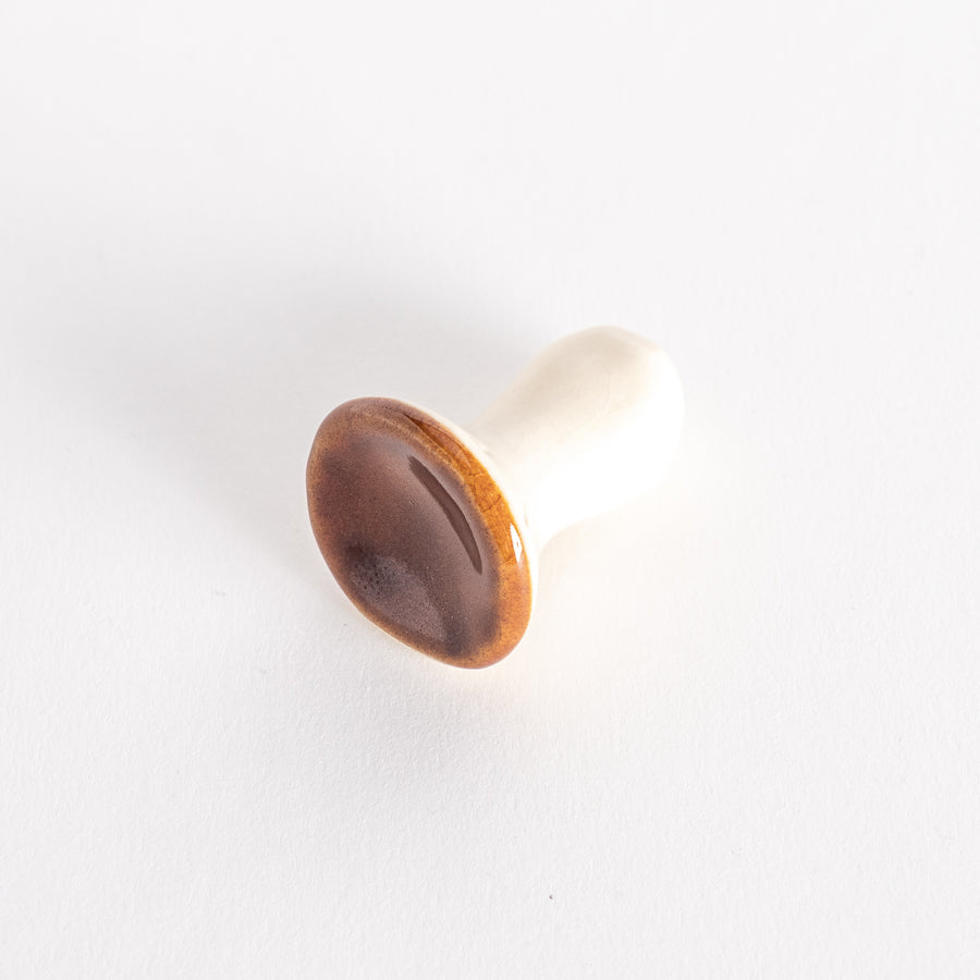 A porcelain chopsticks rest shaped like a porcini mushroom, with a glossy brown cap and smooth white stem.