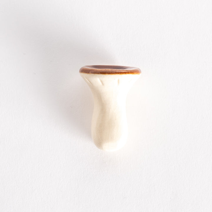 A porcelain chopsticks rest shaped like a porcini mushroom, with a glossy brown cap and smooth white stem.